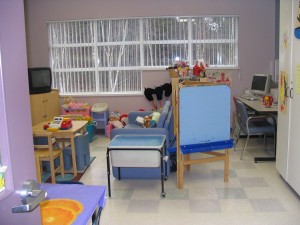 Shelter playroom with a tv, table and chairs, computer, easel and variety of toys.
