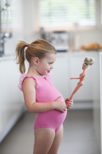 Young girl in dance tricot holding toy fashion doll in kitchen.