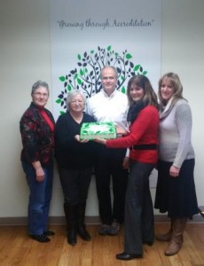 Family Transition Place's Finance Committee members holding a cake smiling together at the camera.