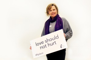 A woman wearing a purple scarf in support of the Wrapped in Courage campaign, holding a sign that says "love should not hurt".