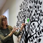 Norah Kennedy putting a green leaf on the accreditation tree in the Family Transition Place boardroom.