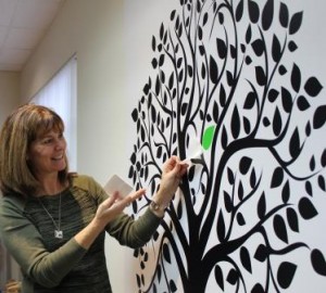 Norah Kennedy putting a green leaf on the accreditation tree in the Family Transition Place boardroom.