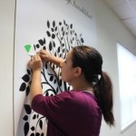 Laura Moscatiello putting a green leaf on the accreditation tree in the Family Transition Place boardroom.