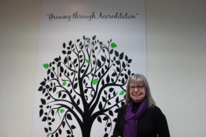 Elaine Capes putting a green leaf on the accreditation tree in the Family Transition Place boardroom.