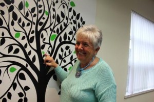 Nancy Mongeon putting a green leaf on the accreditation tree in the Family Transition Place boardroom.