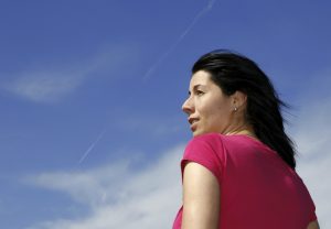 A woman looking off to the side into the distance with blue skies surrounding her.