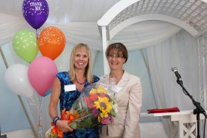 Lyn Allen with Norah Kennedy smiling as Lyn is congratulated for thirty years of service with a bouquet of flowers.