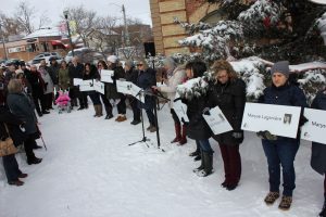 Family Transition Place staff and members of the community taking part in a moment of silence while holding signs with the names of the women who were killed in Montreal during the National Day of Remembrance and Action on Violence Against Women.