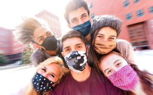 Six young adults wearing masks, huddled together posing happily.
