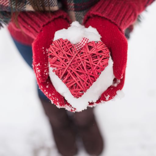 Hands holding snow and red heart.