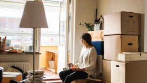 A woman in new apartment, surrounded by unpacked cardboard boxes.