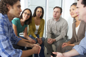 A diverse group of men and women sitting in half circle listening and talking to one another.