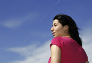 A dark haired woman looking away in front of a blue sky.
