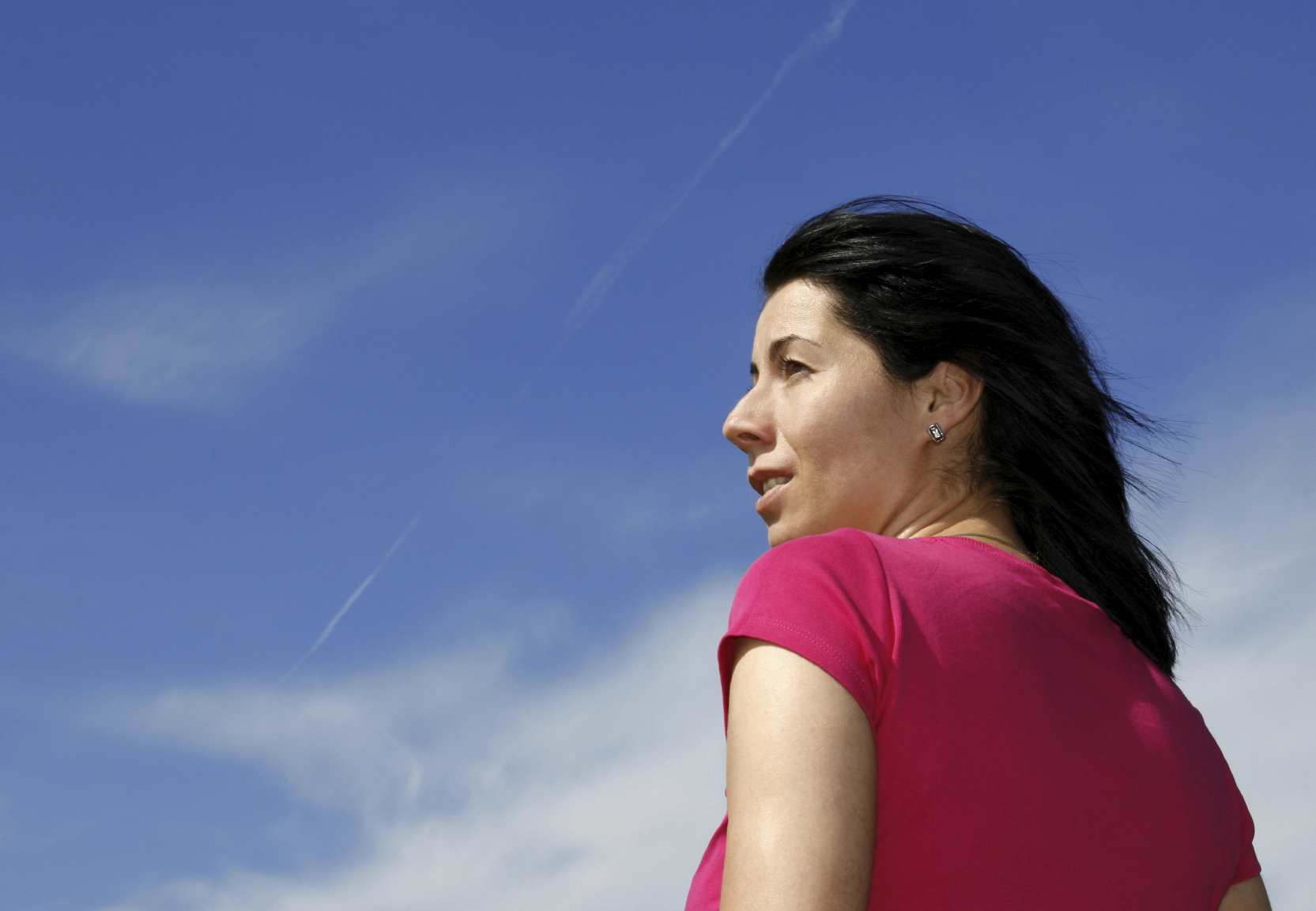 dark haired woman looking away in front of a blue sky