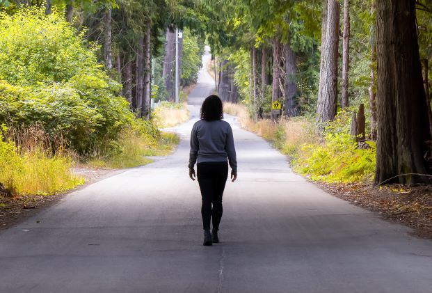 woman walking away from camera down a long road surrounded by trees