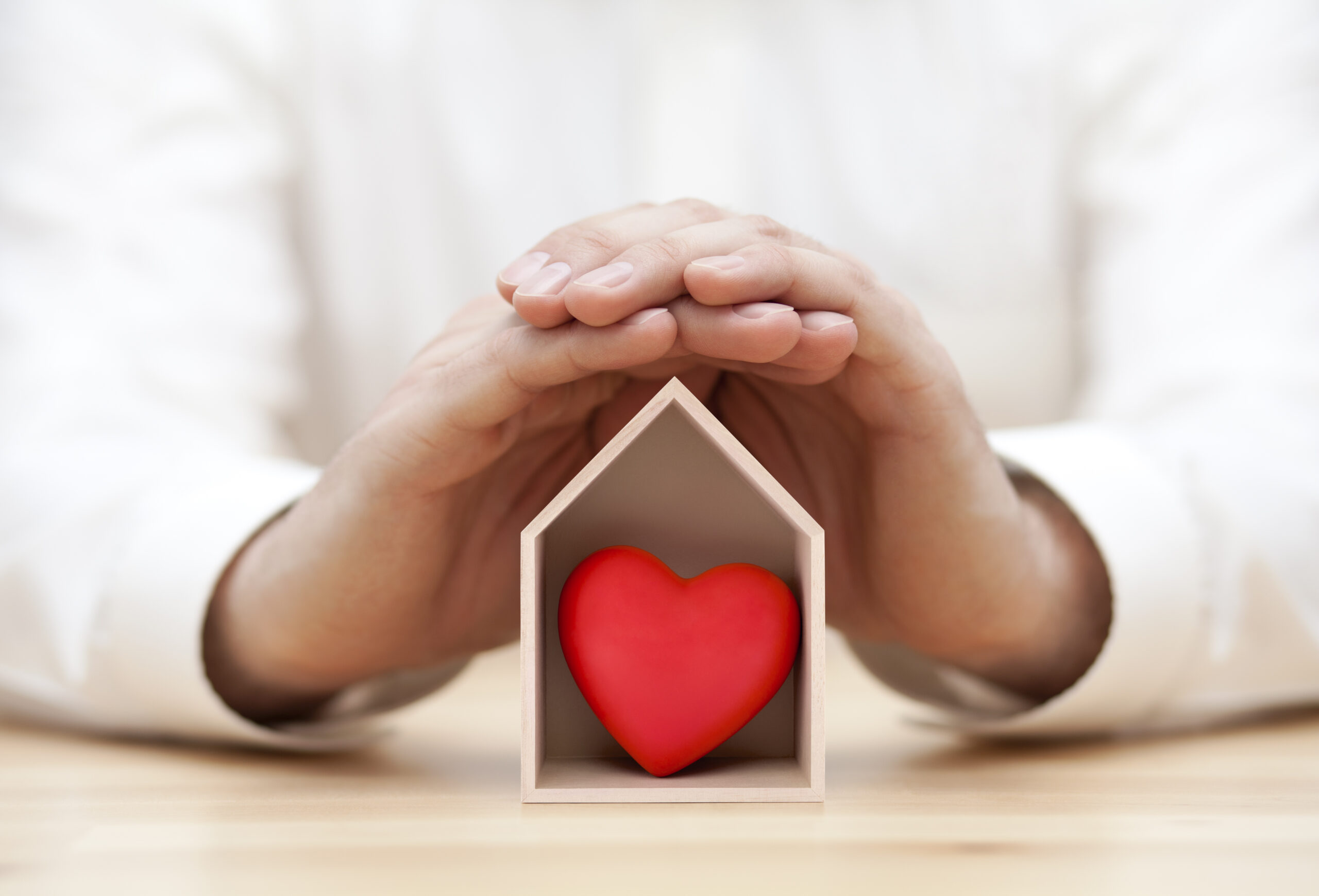 hands covering small white wooden house with red heart inside