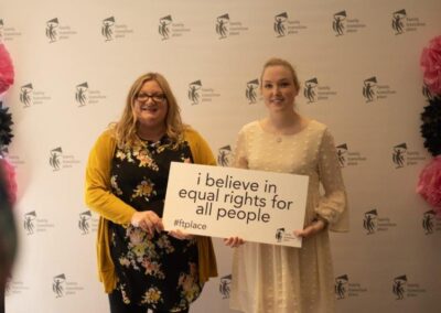 Guests from March 8, 2023 International Women's Day Celebration Luncheon fundraising event holding a sign that says I believe in equal rights for all people.