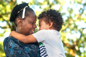 Profile view of an happy black woman hugging her child in nature