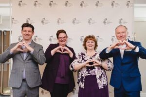 Guests in front of media wall doing heart hand pose at 2024 International Women's Day Celebration Event