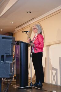Norah Kennedy behind lectern on stage at 2024 International Women's Day Celebration Event